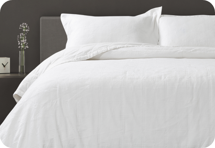 An all-white checkered quilt dressing a queen bed with matching pillow shams.