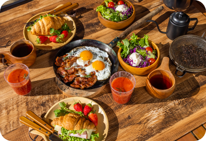 A variety of healthy, balanced breakfast plates on a wooden table out in the sunlight.