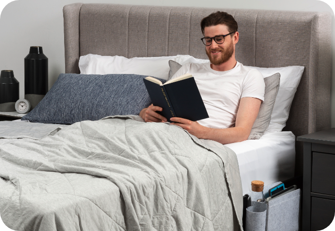 A young man reading in a bed dressed in grey and white tones.