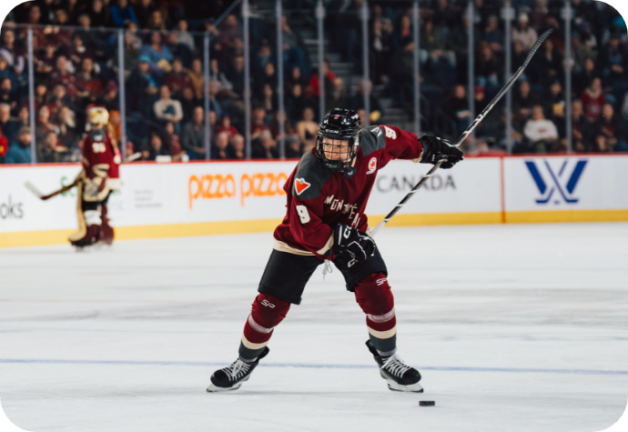 Hockey player Kati Tabin in the official PWHL Montreal maroon and beige attire skating on the ice, poised to take a shot. 